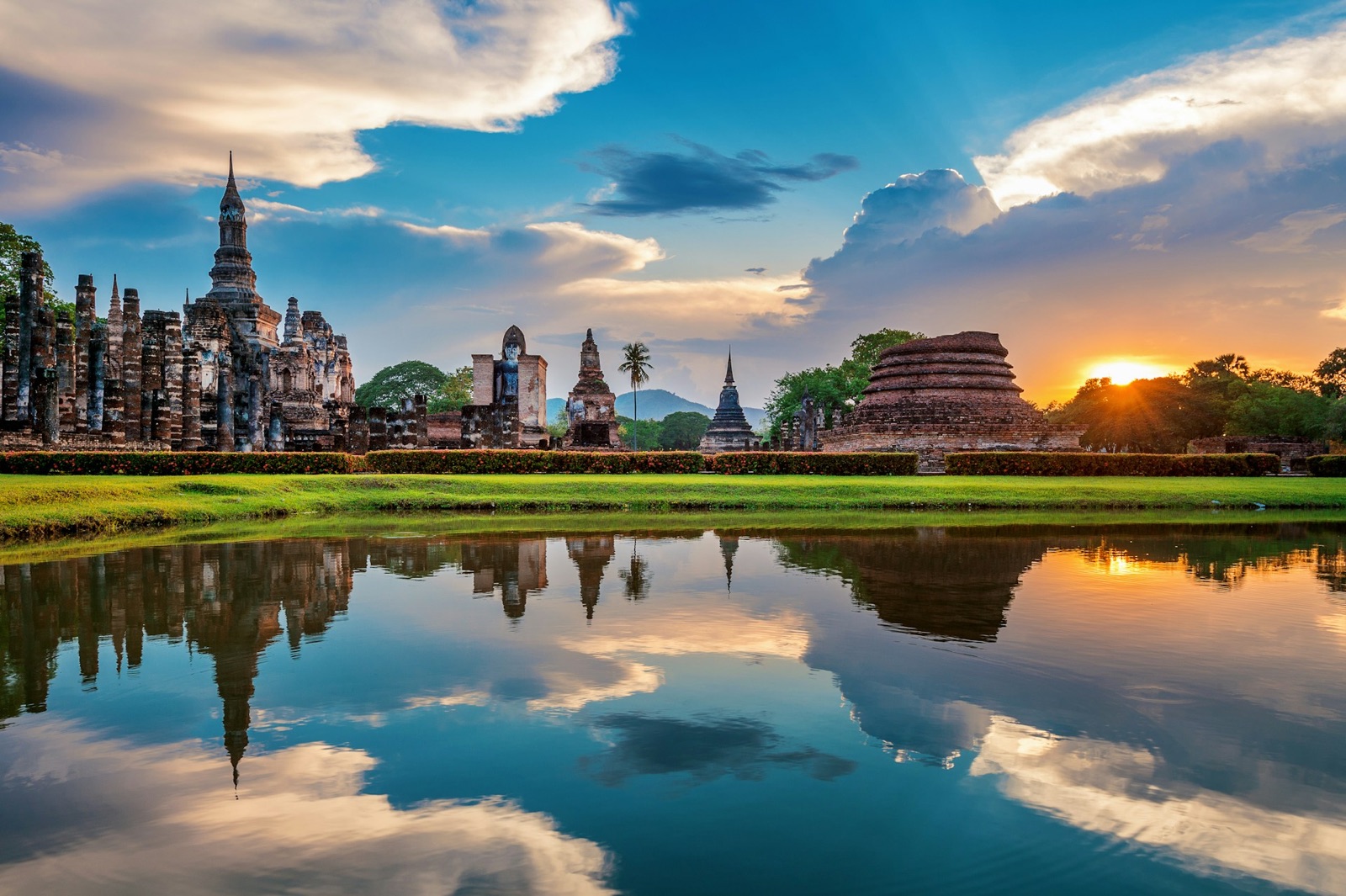 Temple ruins reflected in still water at sunset in Thailand