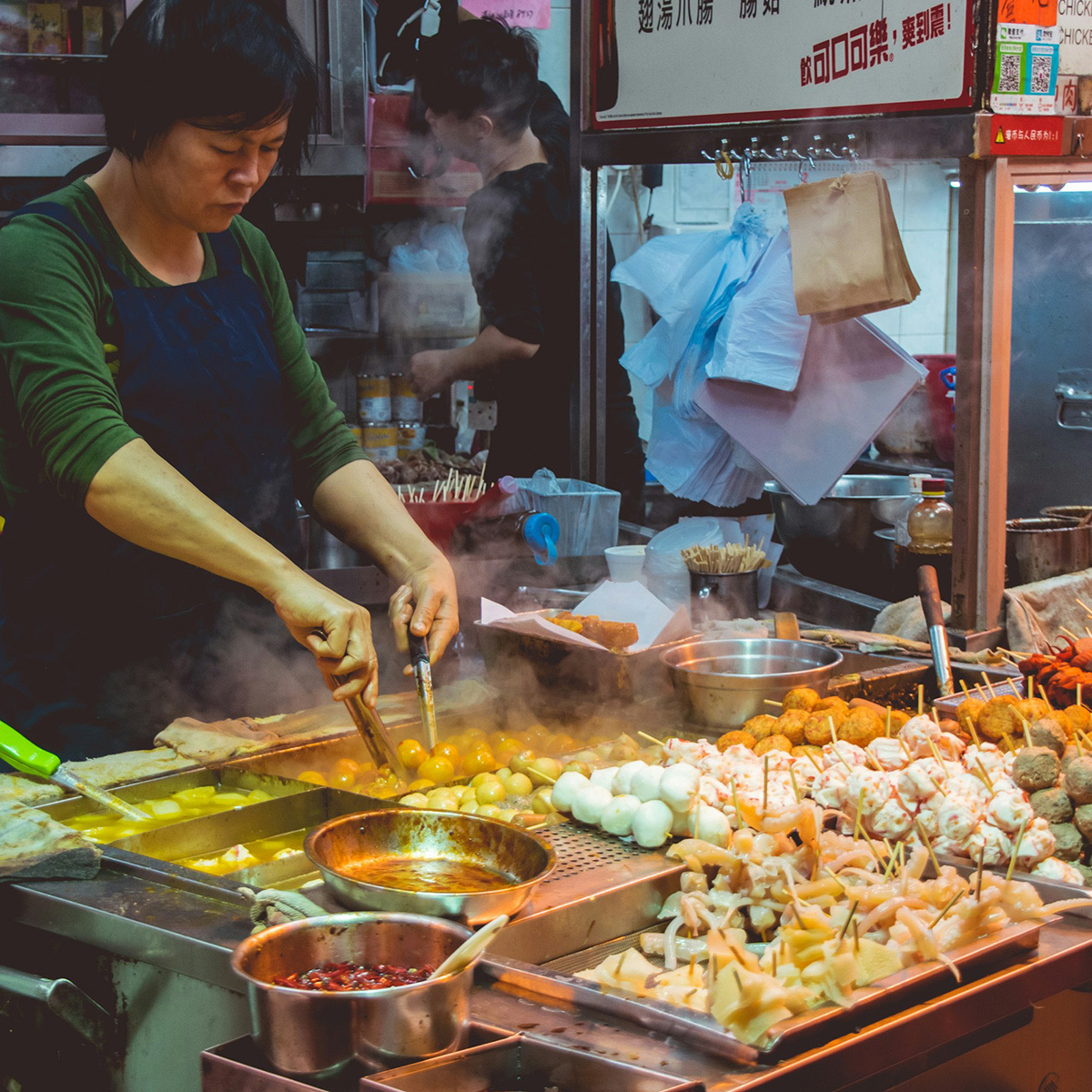 A cook working a street food stall, skewers and steam