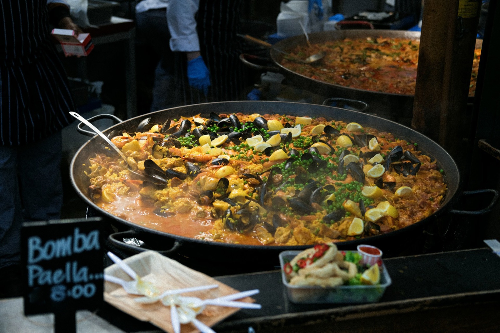 Two wide pans of seafood paella cooking at a market stall