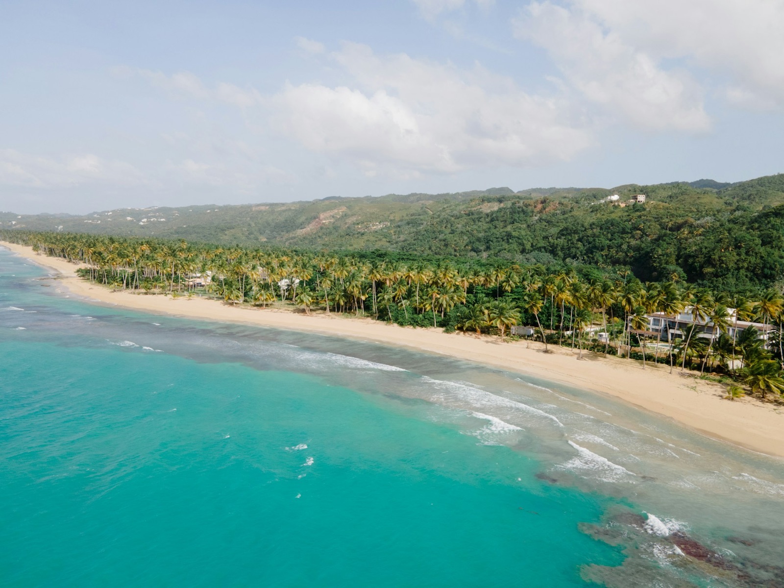 A palm-backed beach and turquoise shallows seen from the air