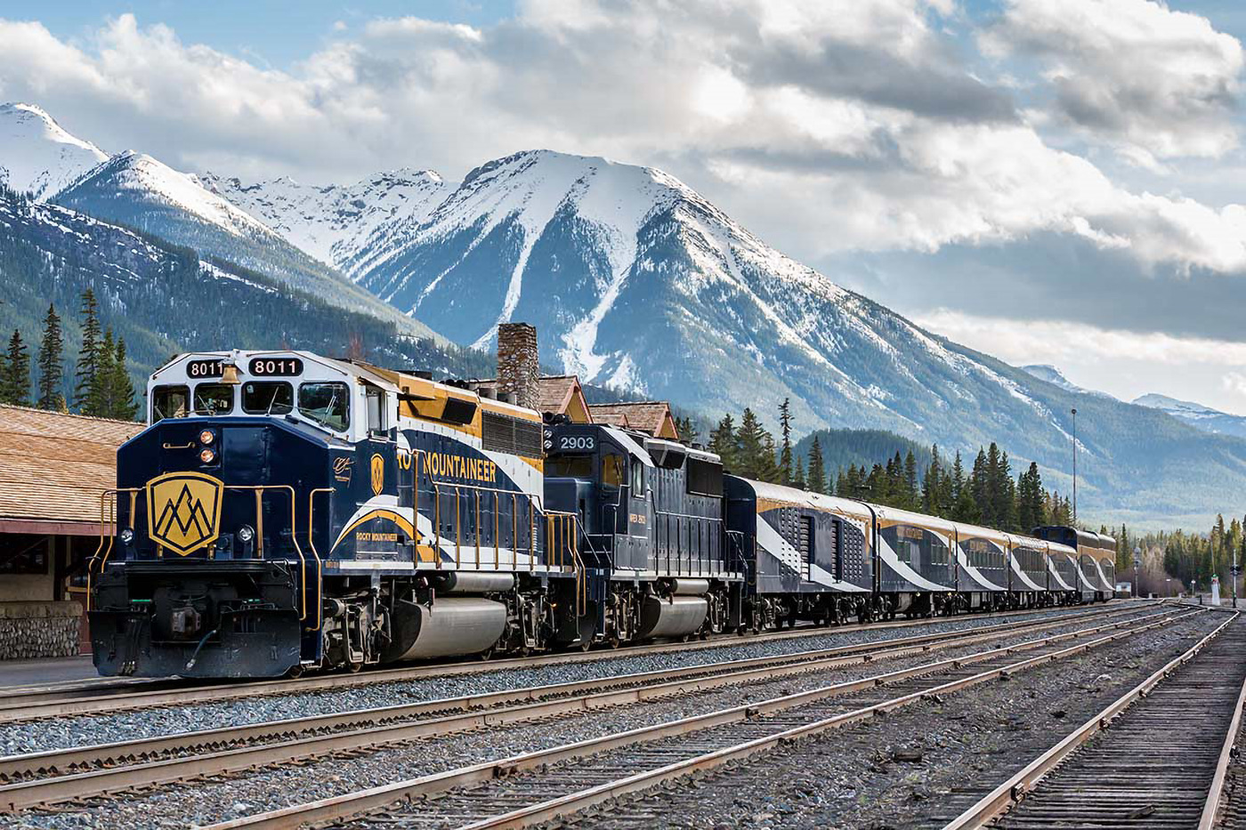 A passenger train waiting below snow-covered peaks in the Canadian Rockies
