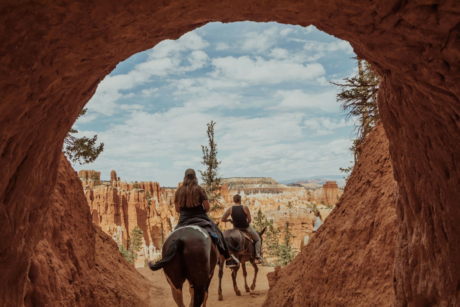 Riders on horseback passing through a rock arch above the Bryce hoodoos