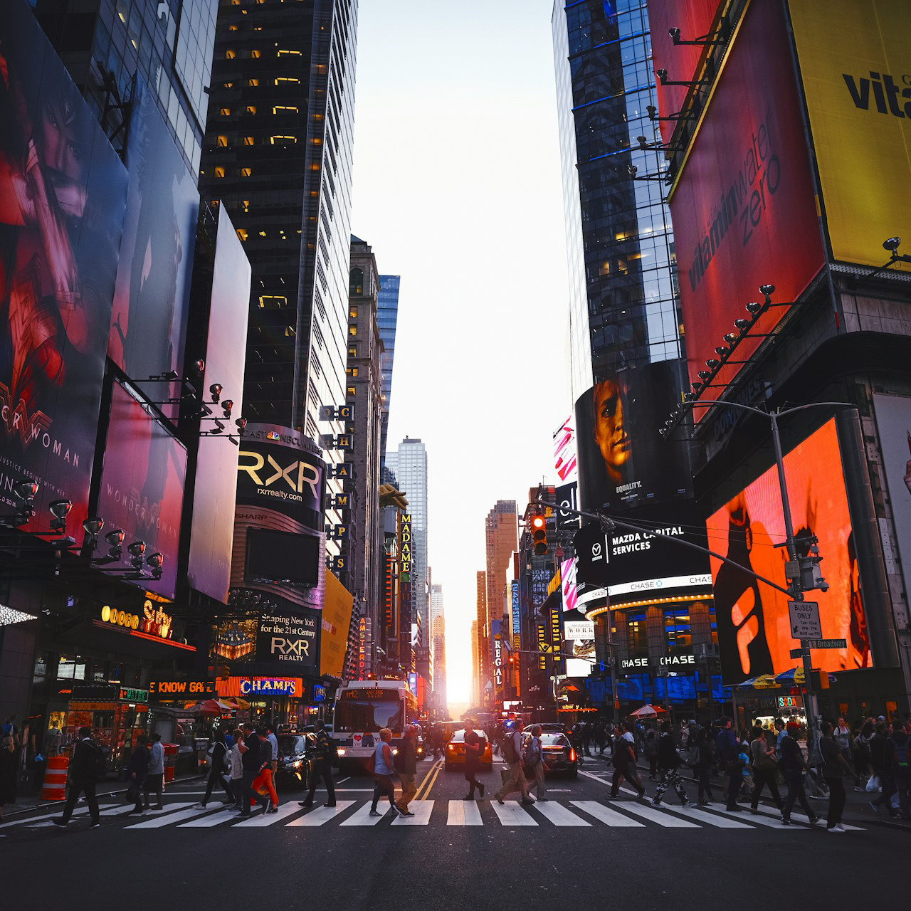 A crowded Manhattan crossing at street level with the sun down the avenue