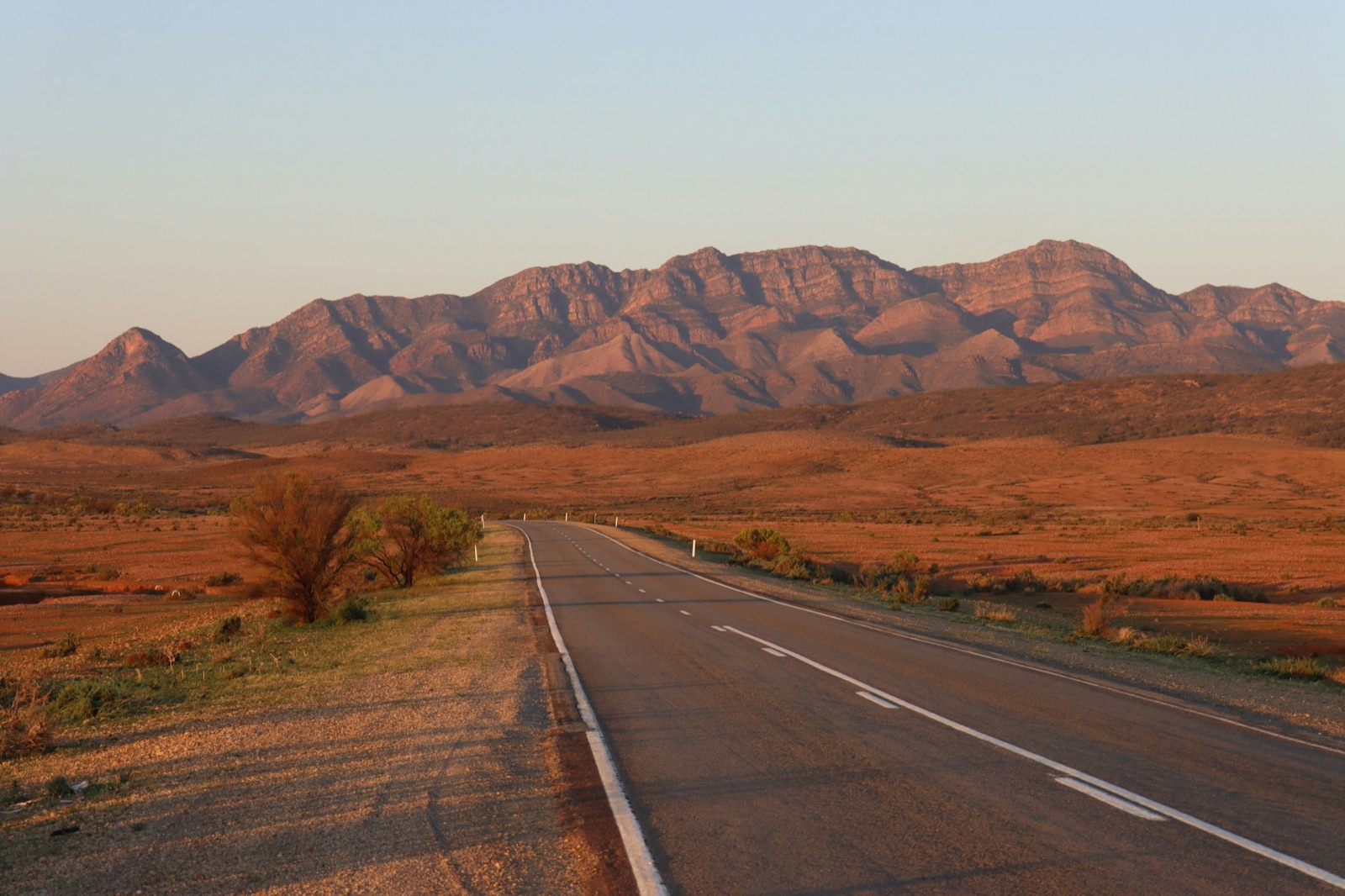 An empty road running toward red ranges in the late Australian light