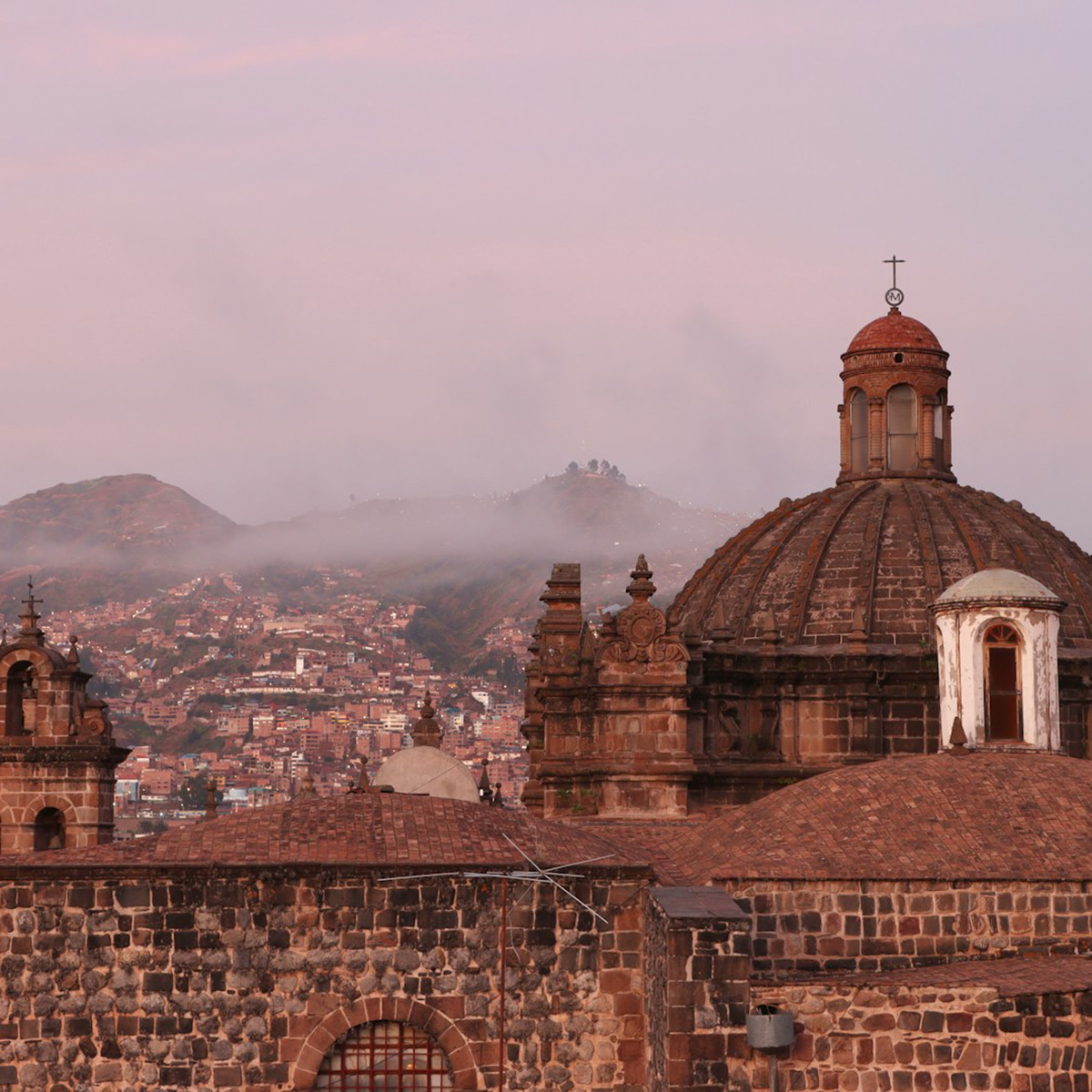 Cusco rooftops and domes at dusk with mist on the hills behind