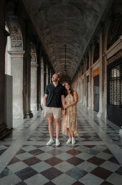 Two travelers in the colonnade at St Mark's Square, Venice