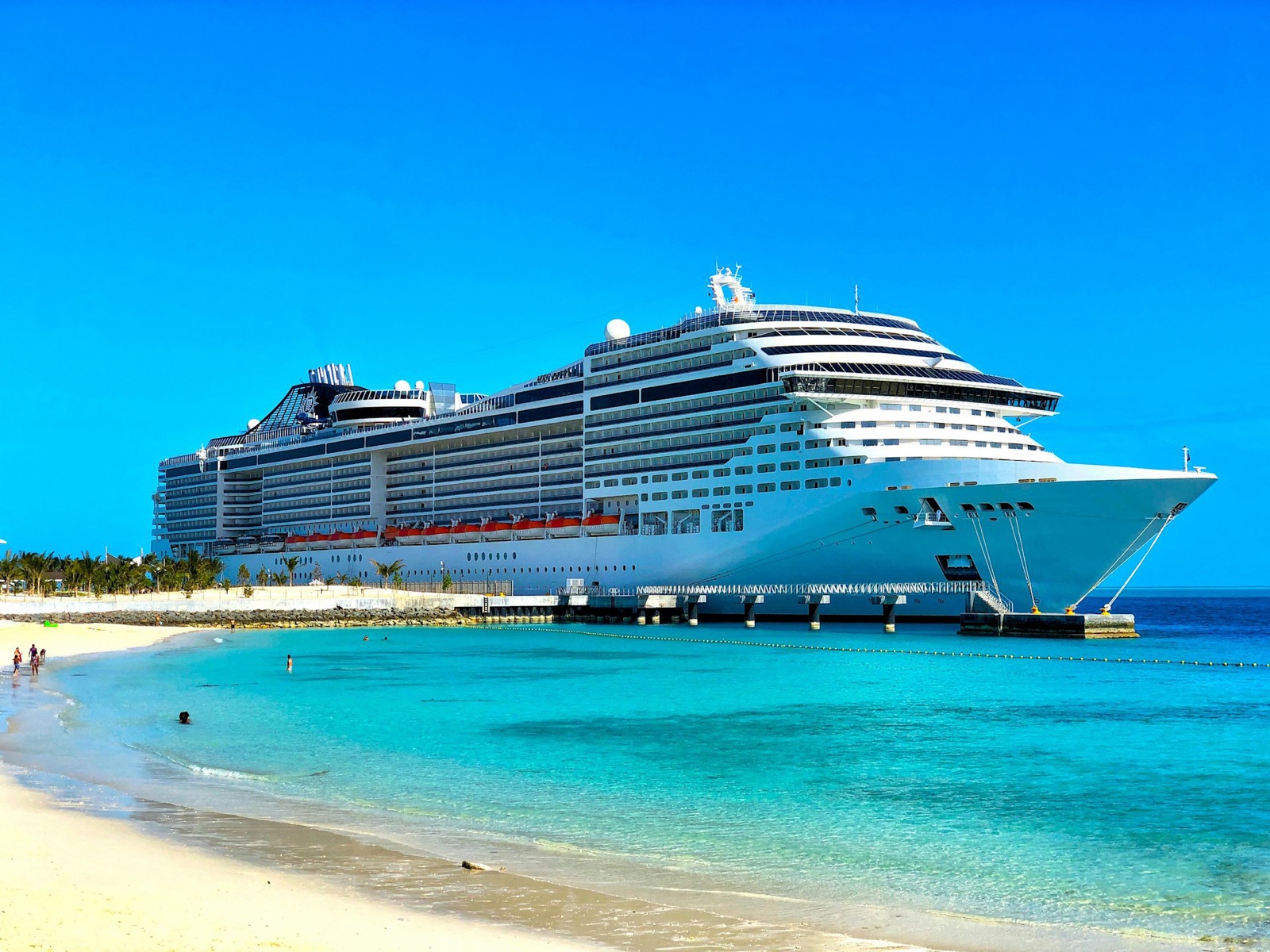 A cruise ship alongside a pier with turquoise water and a beach in front of it